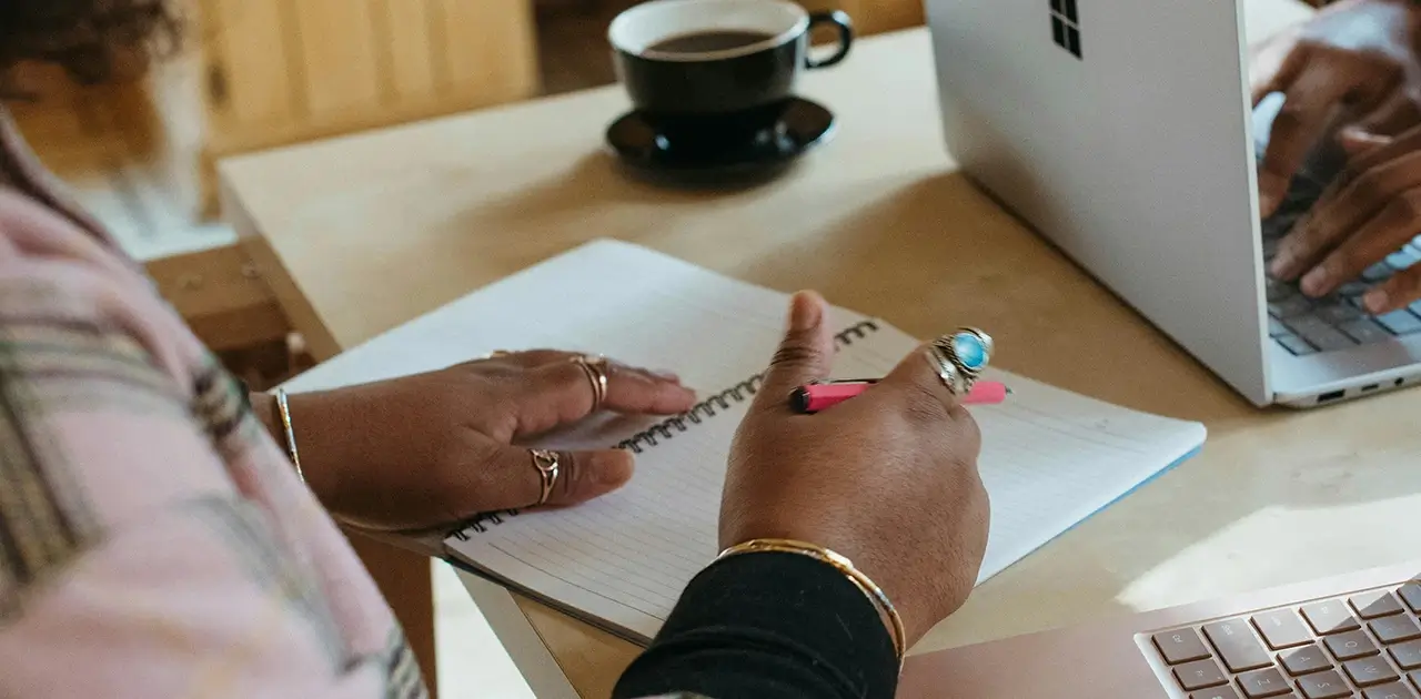 Woman writing in notebook next to someone typing